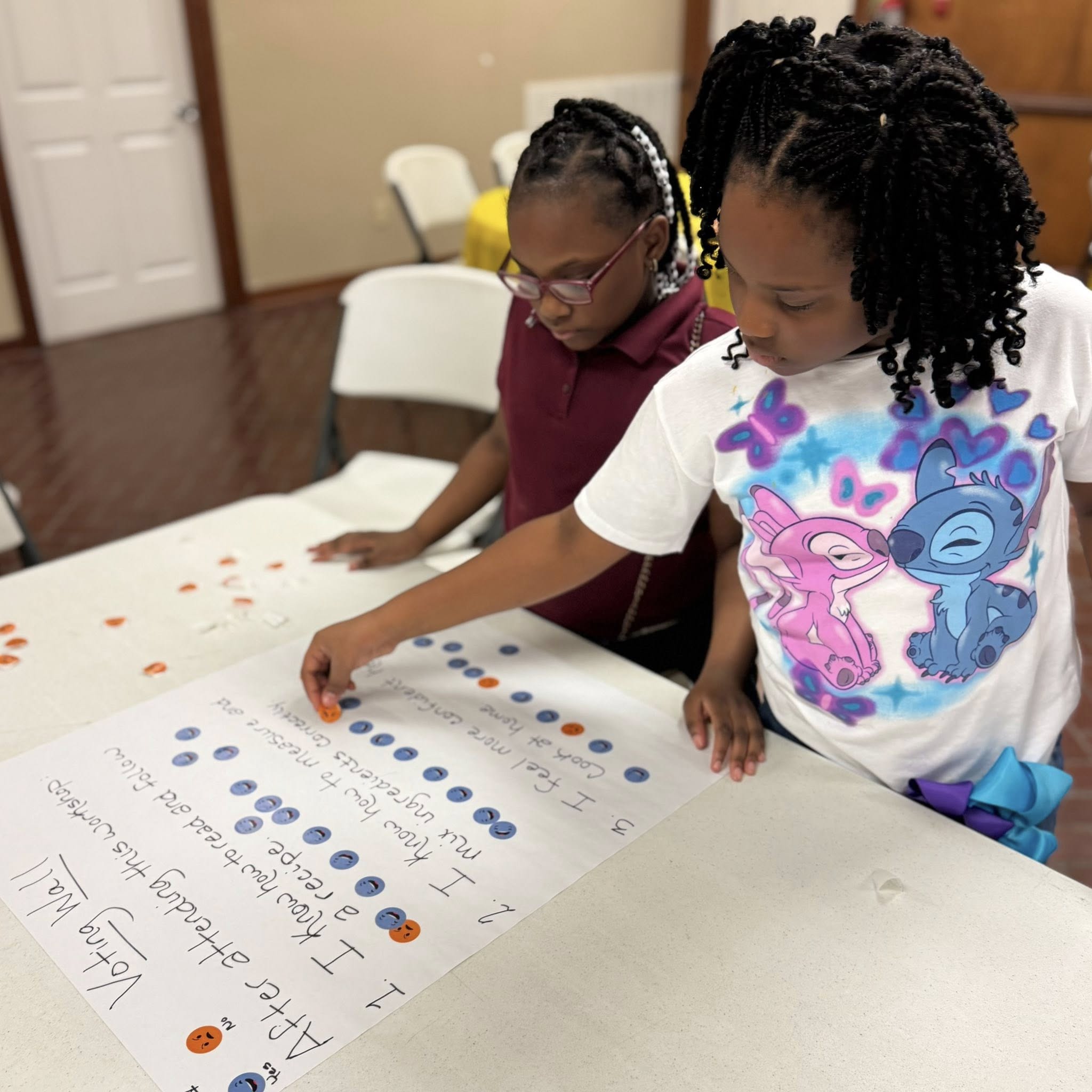 Two girls reading a poster on a table.